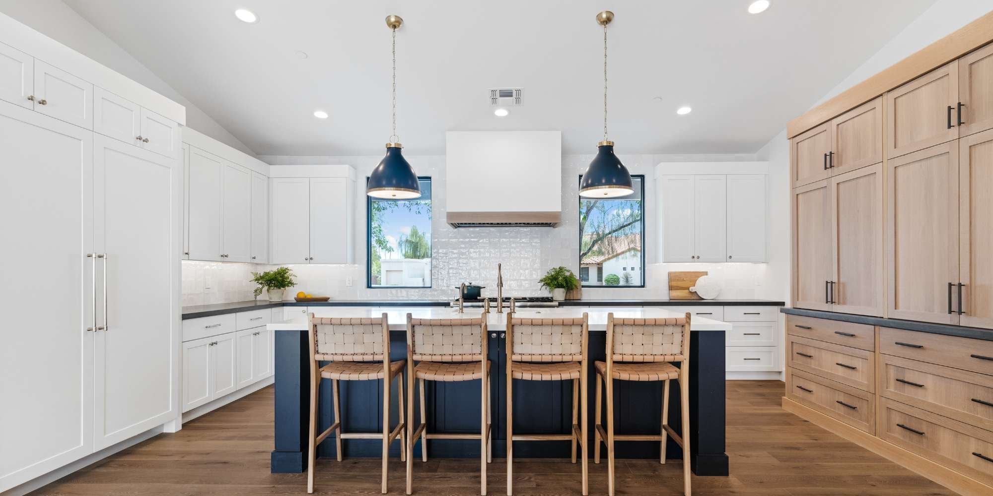 Modern kitchen remodel with white cabinets, wood accents, navy island, and pendant lighting by Trinity Homes