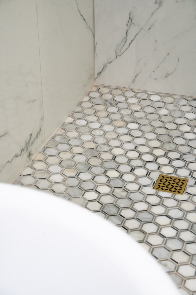Marble shower floor with hexagon tile and brass drain in Phoenix bathroom remodel by Trinity Homes