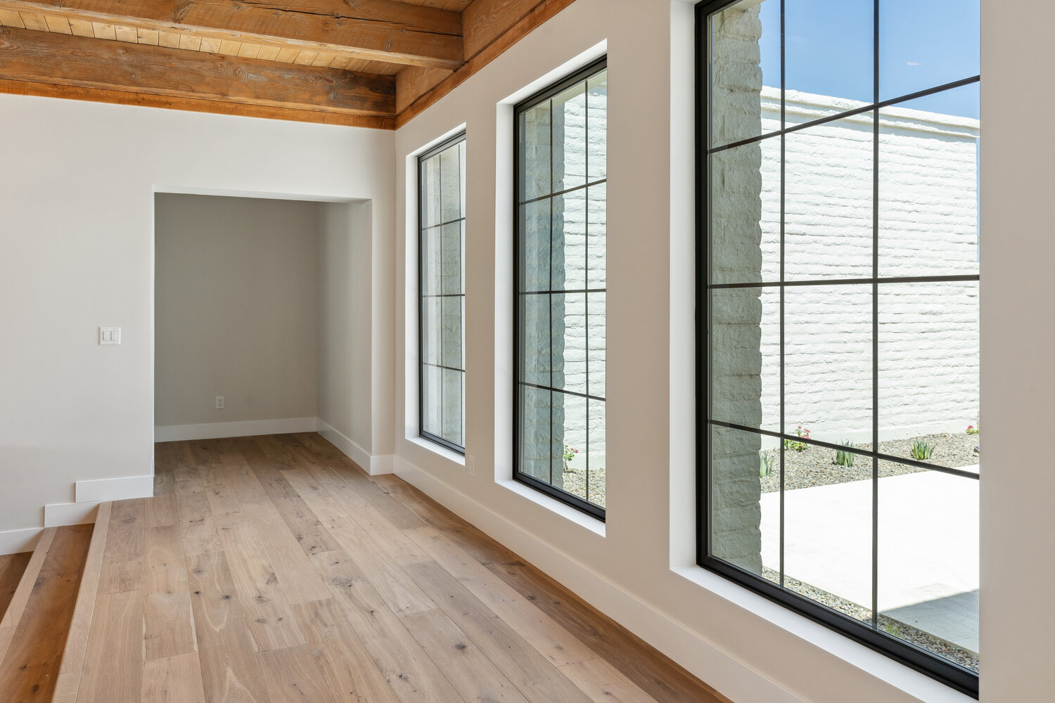 Light-filled hallway with wood floors and black grid windows by Trinity Homes in Paradise Valley