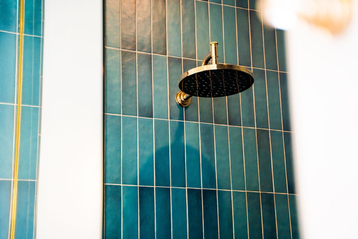 Brass rain showerhead against vertical teal tile wall in a Trinity Homes AZ custom bathroom in Scottsdale, AZ