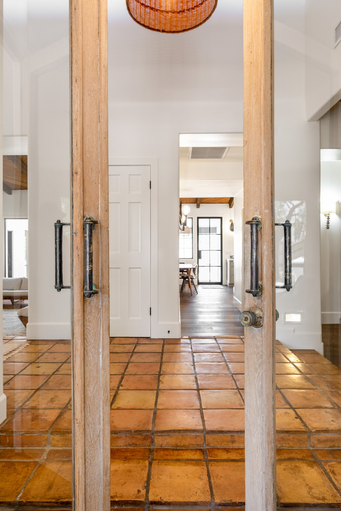 Glass entry doors opening to tile-floored interior with wood ceiling details by Trinity Homes in Scottsdale, AZ