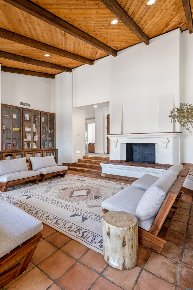 Living room with wood beam ceiling, white fireplace, and terracotta tile in a Scottsdale home by Trinity Homes