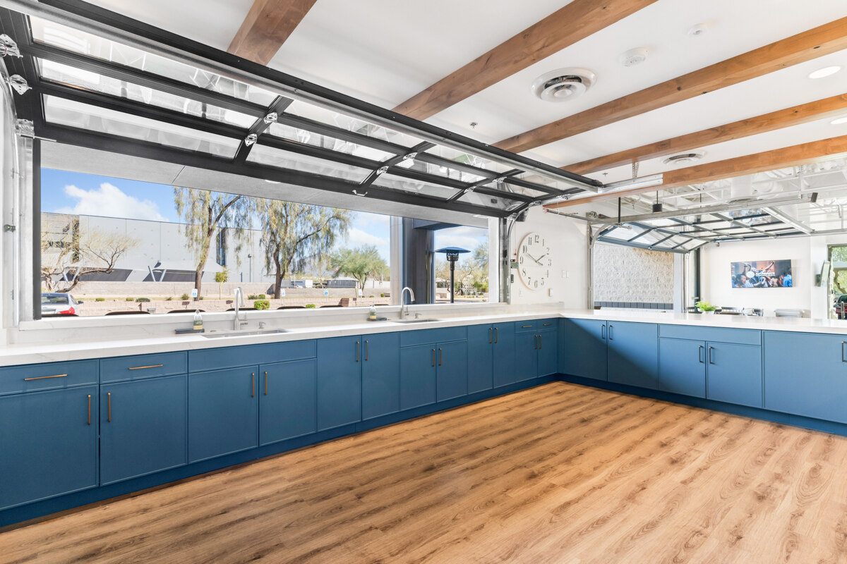 Corner kitchen area with blue cabinets and open garage windows by Trinity Homes in Scottsdale