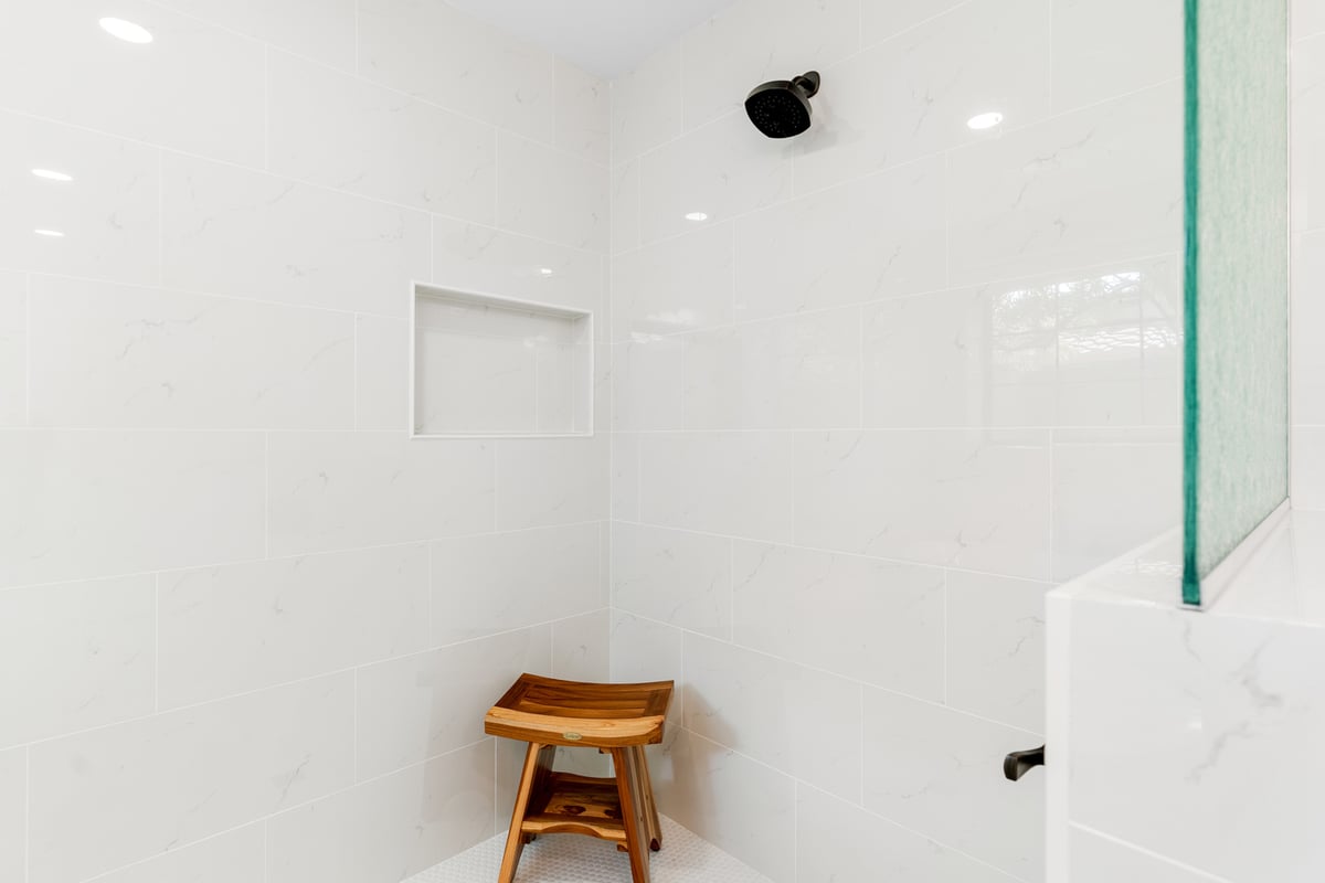 Custom tiled walk-in shower with black showerhead and teak bench in a Trinity Homes AZ project in Cave Creek AZ