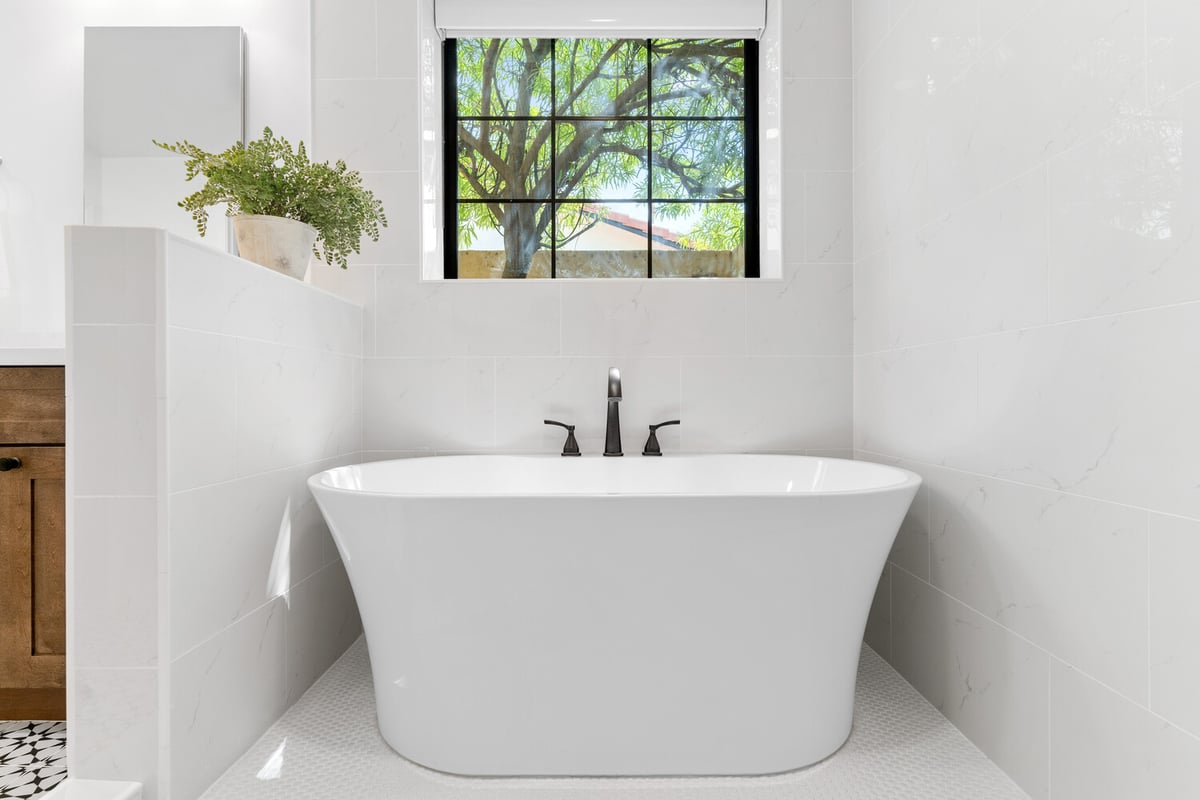 Freestanding soaking tub beneath large window in luxury bathroom by Trinity Homes AZ in Mesa, AZ