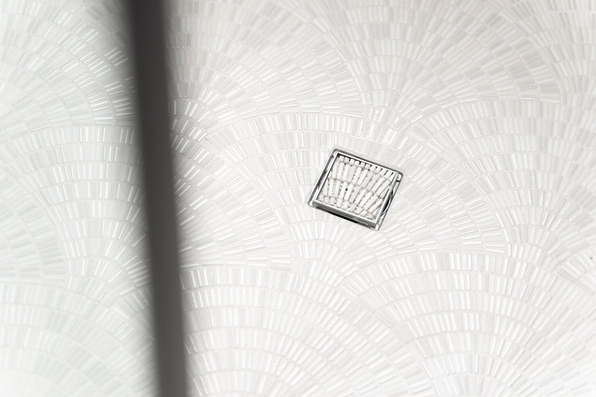 Close-up of white mosaic shower tile with decorative drain by Trinity Homes AZ in Scottsdale, AZ
