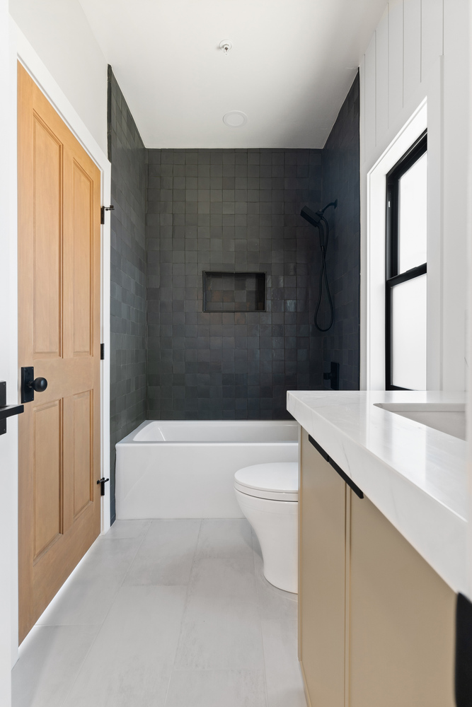 Custom bathroom design with dark tile, white tub, and oak door by Trinity Homes AZ in Scottsdale