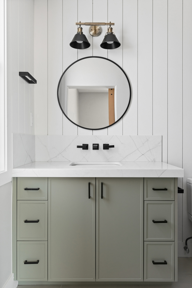 Elegant custom bathroom with sage green vanity and circular mirror by Trinity Homes AZ in Cave Creek, AZ
