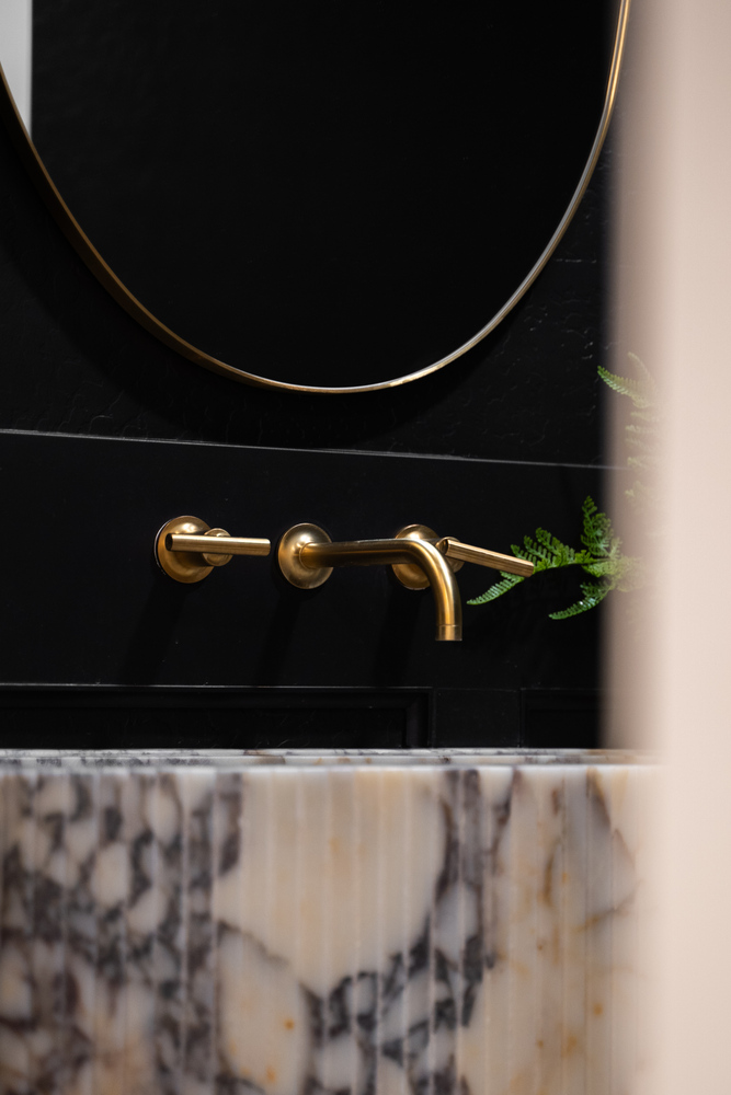 Brass bathroom faucet with black and marble design in Trinity Homes remodel in Gilbert, AZ