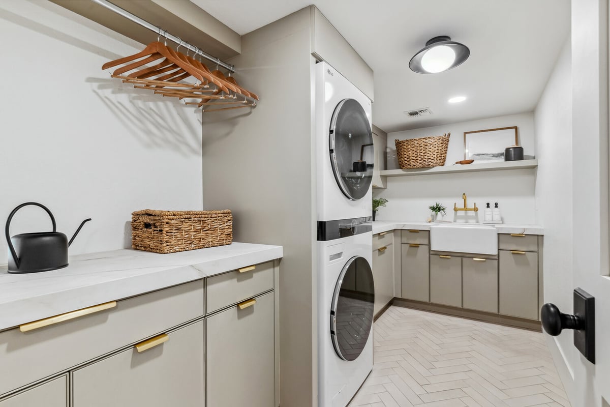 Stylish laundry room with stacked washer-dryer and farmhouse sink by Trinity Homes in Gilbert, AZ
