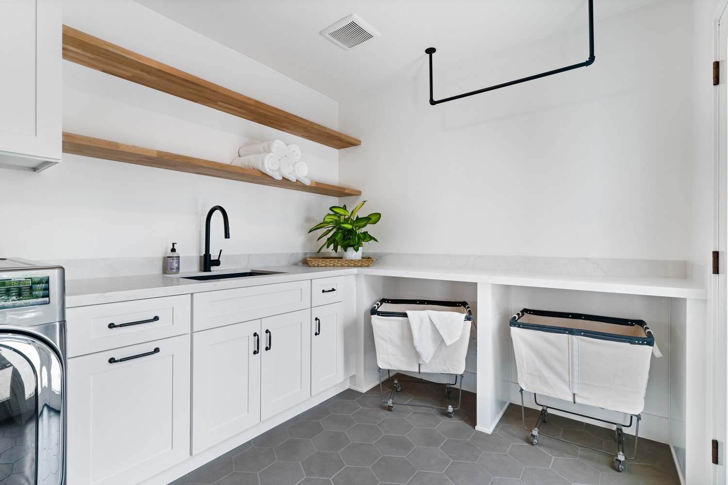 Bright laundry room with white cabinets, black fixtures, and laundry carts by Trinity Homes AZ in Chandler, AZ